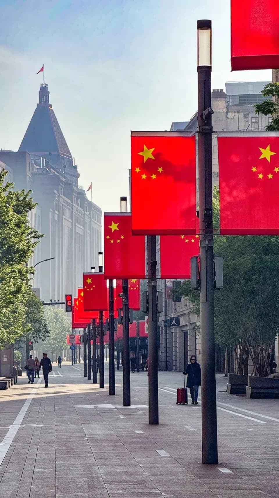 Chinese national flags hang from a row of street lamps beside a stone-paved city street