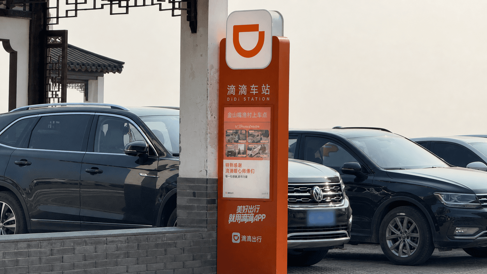 An orange DiDi Station sign beside parked cars in Jinshanzui Fishing Village, Shanghai