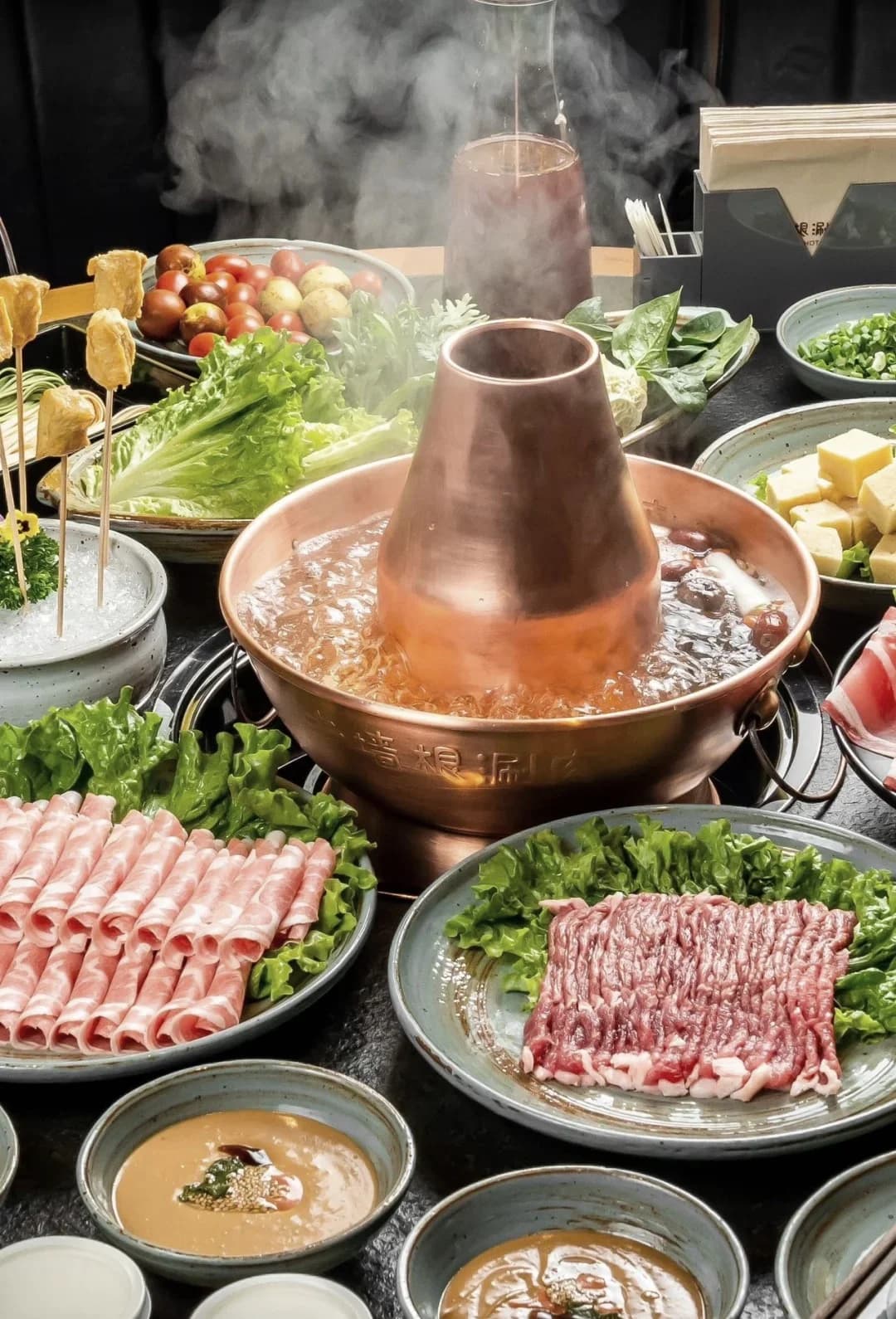 Copper hotpot surrounded by sliced meat, vegetables and dipping sauces