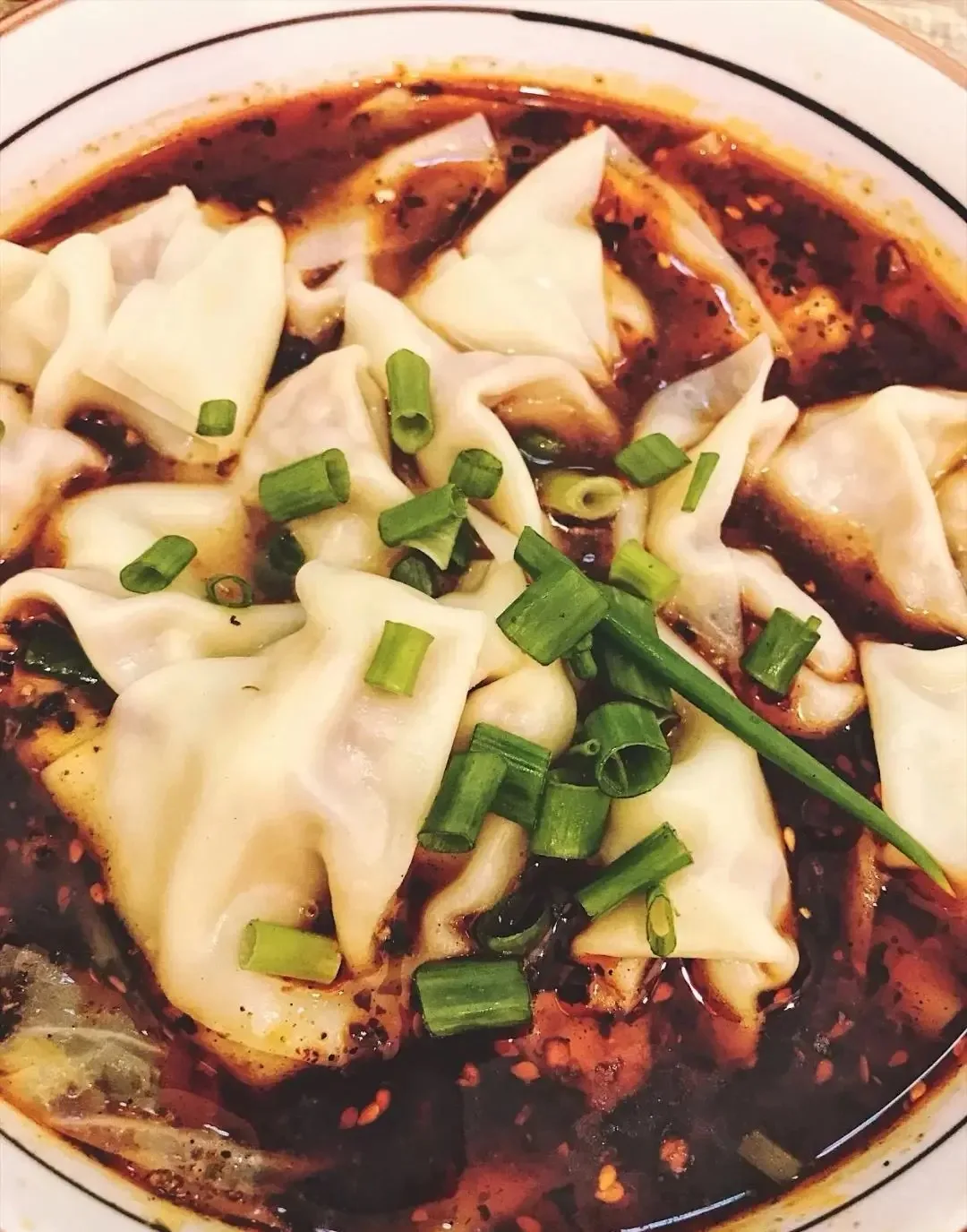 Folded wontons in red chili oil topped with chopped green onions.
