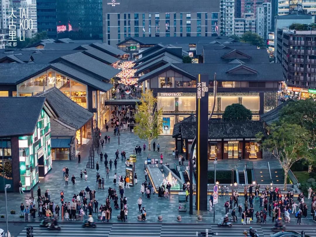 An elevated evening view of Taikoo Li Chengdu, with tiled roofs, lit shopfronts and the original Taikoo Li logo in the upper left.