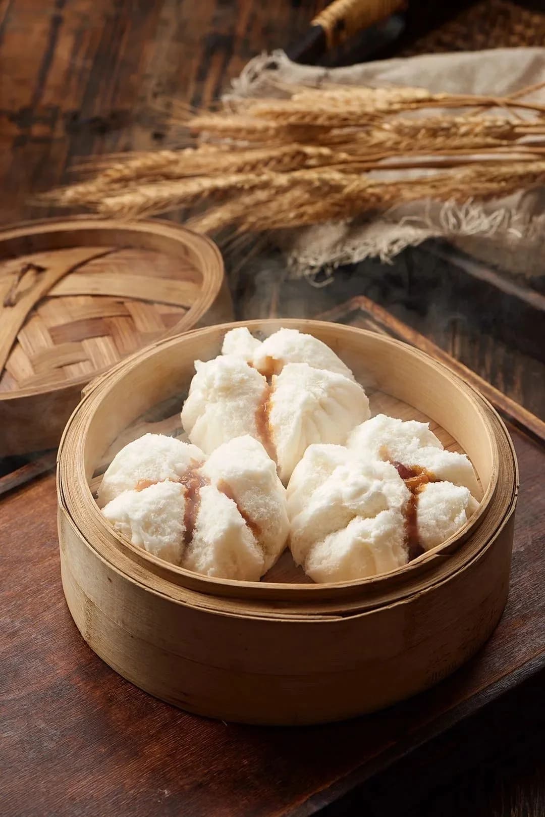 Three white steamed buns with split tops and visible filling in a bamboo steamer.