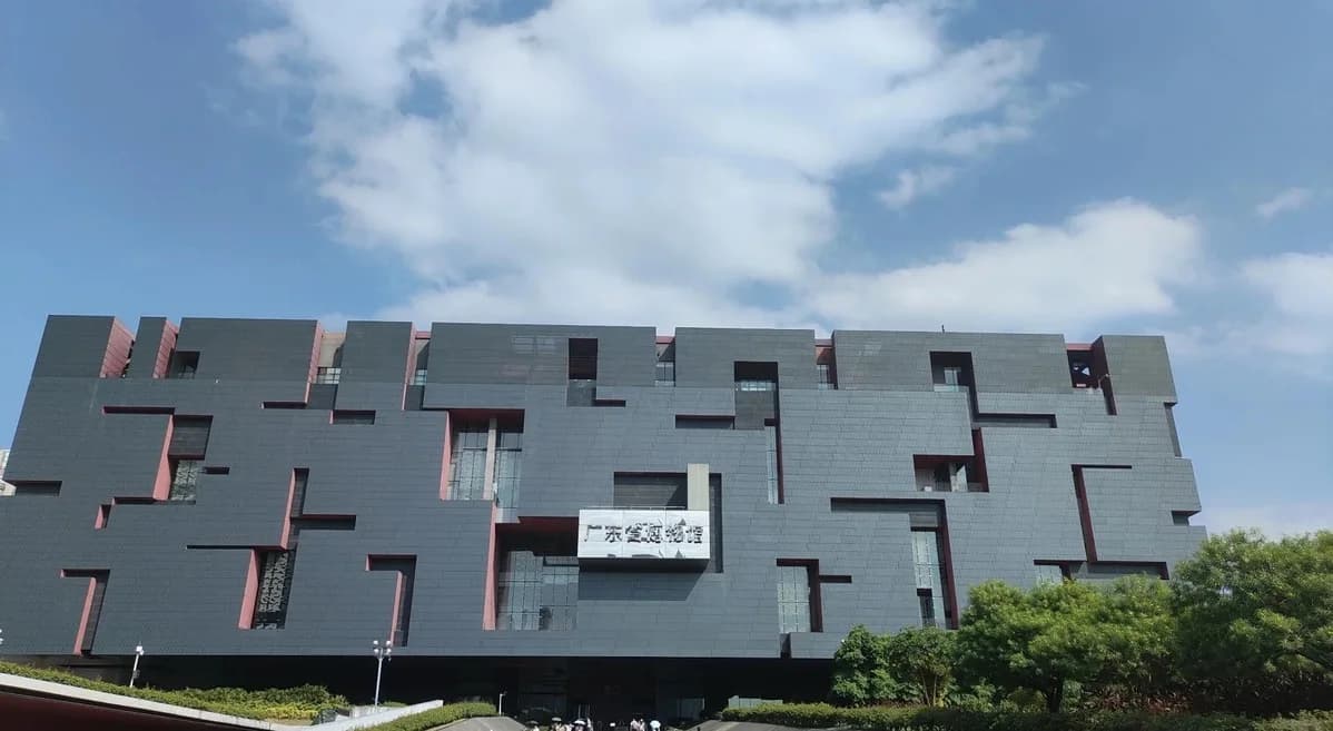 The block-shaped facade of Guangdong Museum beneath a cloudy blue sky.
