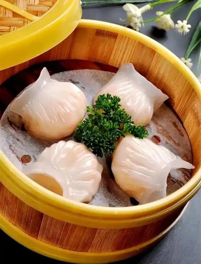 Four translucent shrimp dumplings in a bamboo steamer with a green garnish.