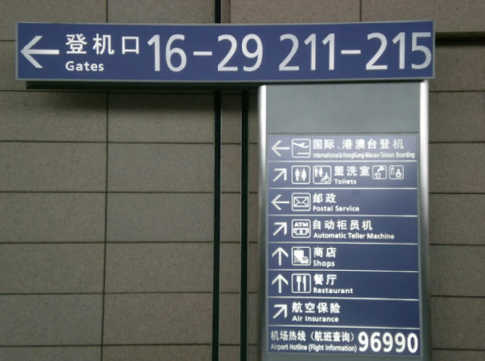 Blue bilingual signs pointing to boarding gates, toilets, an ATM and other airport services.
