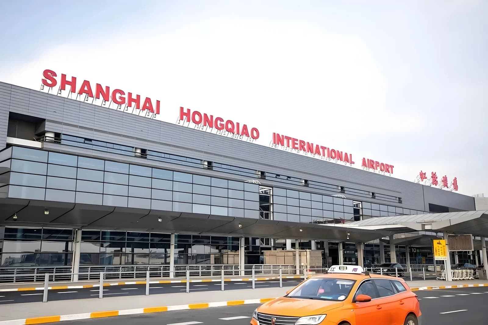 Shanghai Hongqiao International Airport lettering above the terminal, with an orange taxi in front.