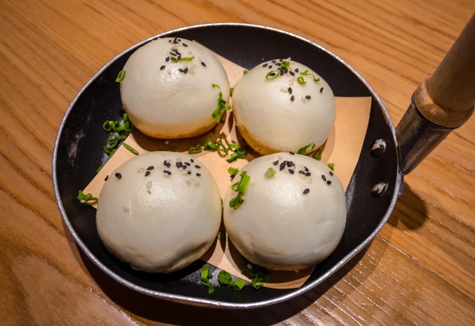 Four whole pan-fried buns with sesame seeds and scallions in a black pan.