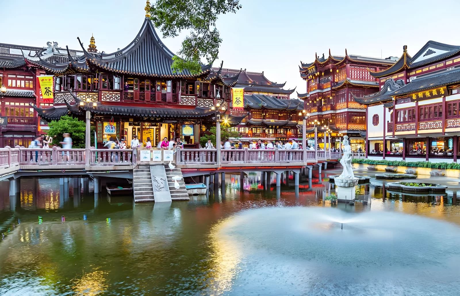 A traditional pavilion, a pedestrian bridge and red-fronted buildings around a pond in the Yuyuan area.
