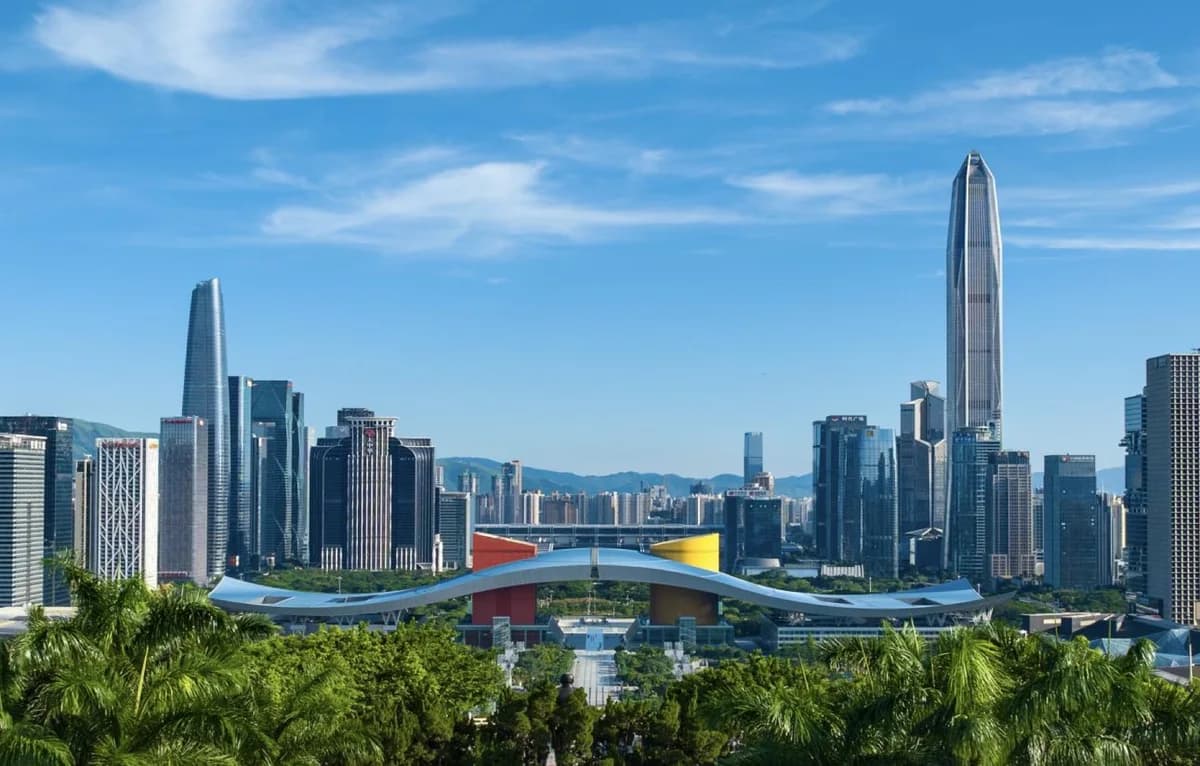 The broad curved roof of Shenzhen Civic Center with trees in front and high-rises behind it.