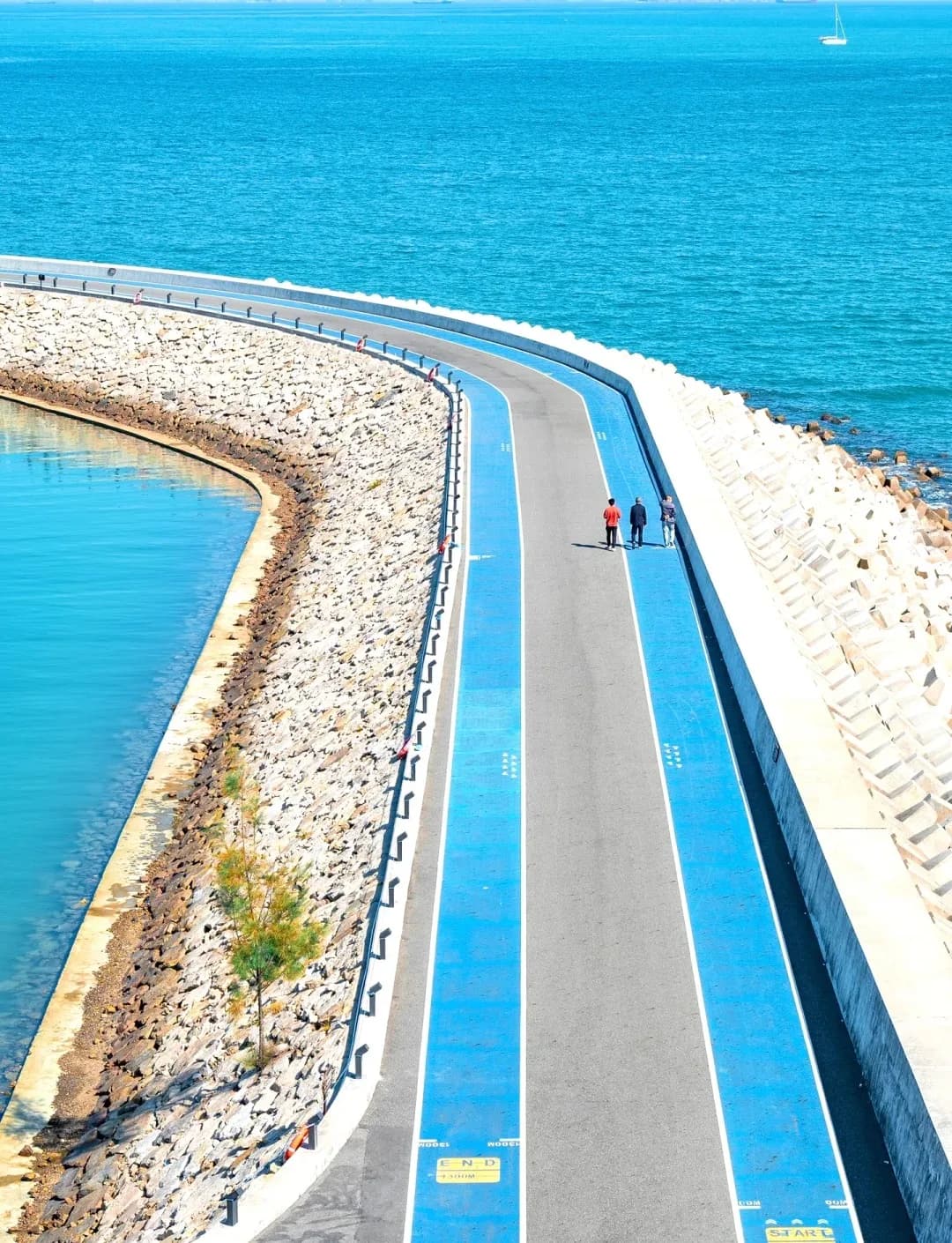 A curved breakwater walkway edged in blue beside the sea at Langqi in Shenzhen’s Dapeng New District.