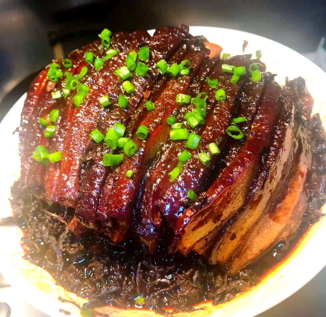 Glossy slices of pork belly over dark preserved greens, topped with chopped spring onion.