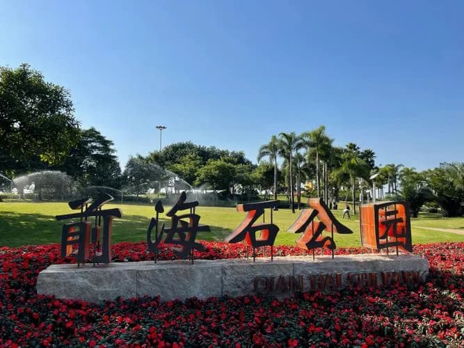 Large Chinese characters spelling Qianhai Stone Park above a stone base, surrounded by flowers and palms.