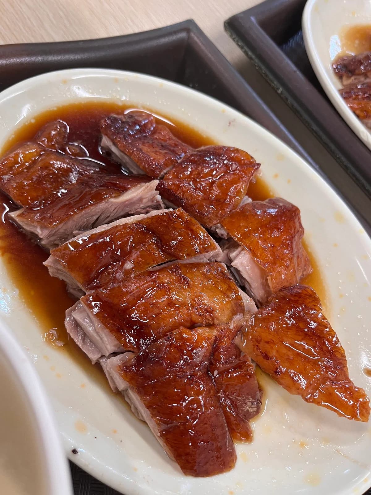 Sliced roast goose with glossy brown skin and sauce on an oval white plate.