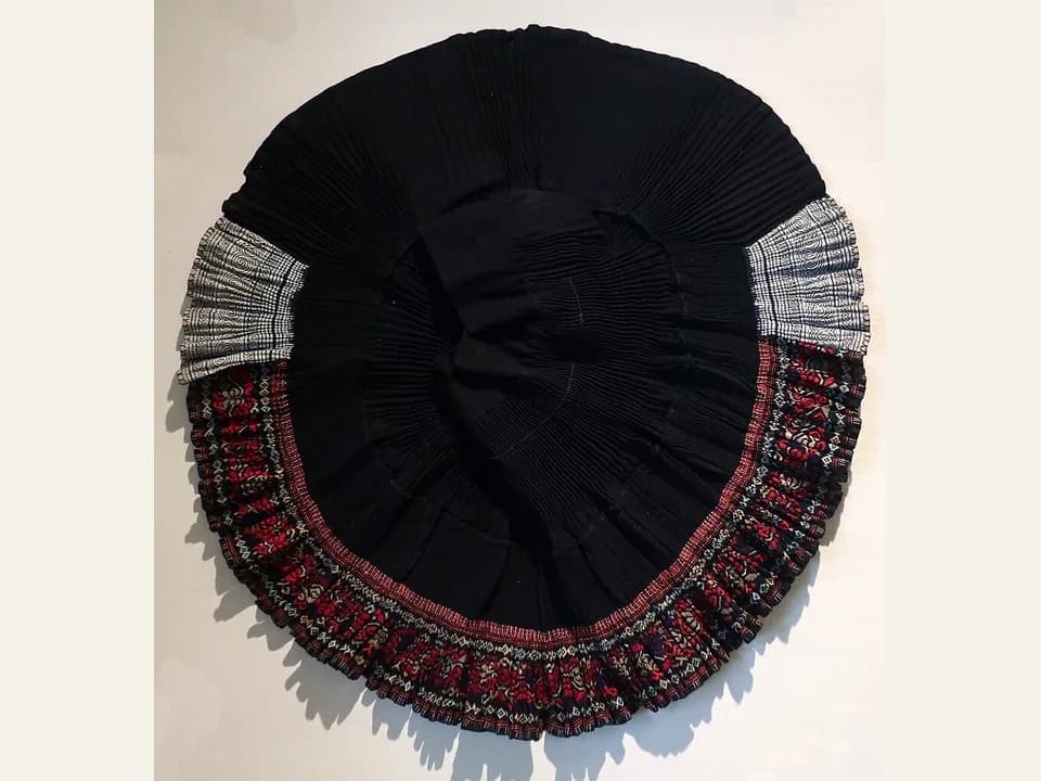 Black pleated Miao festival skirt with wax-resist, indigo and embroidered patterned bands displayed in a museum