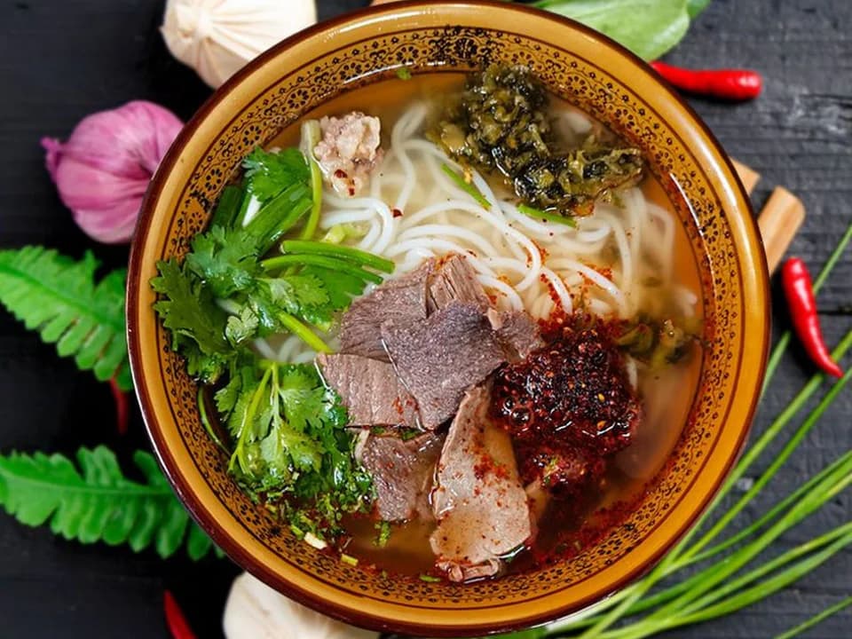 Guizhou beef rice noodles with sliced beef, chili and cilantro in a patterned bowl