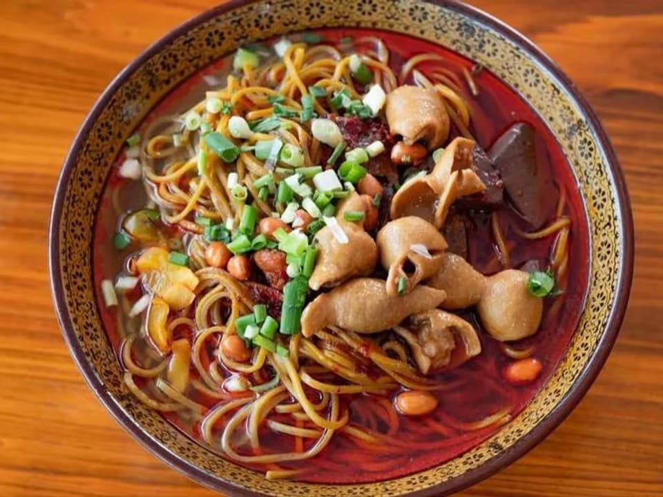 Overhead view of Guiyang Changwang noodles with pork intestine, blood curd, peanuts and scallions in red broth