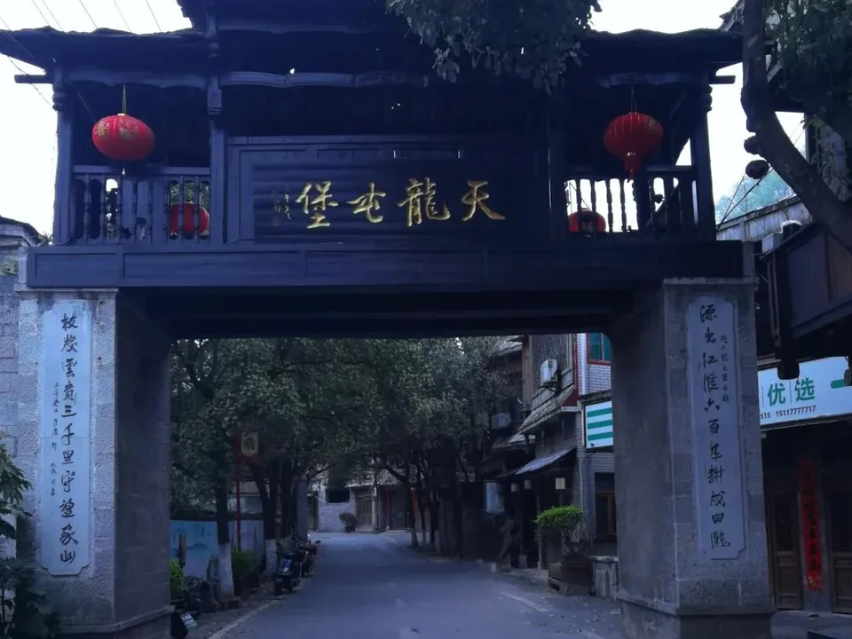 Dark wooden Tianlong ancient fortress gate with red lanterns above a quiet street near Anshun in Guizhou