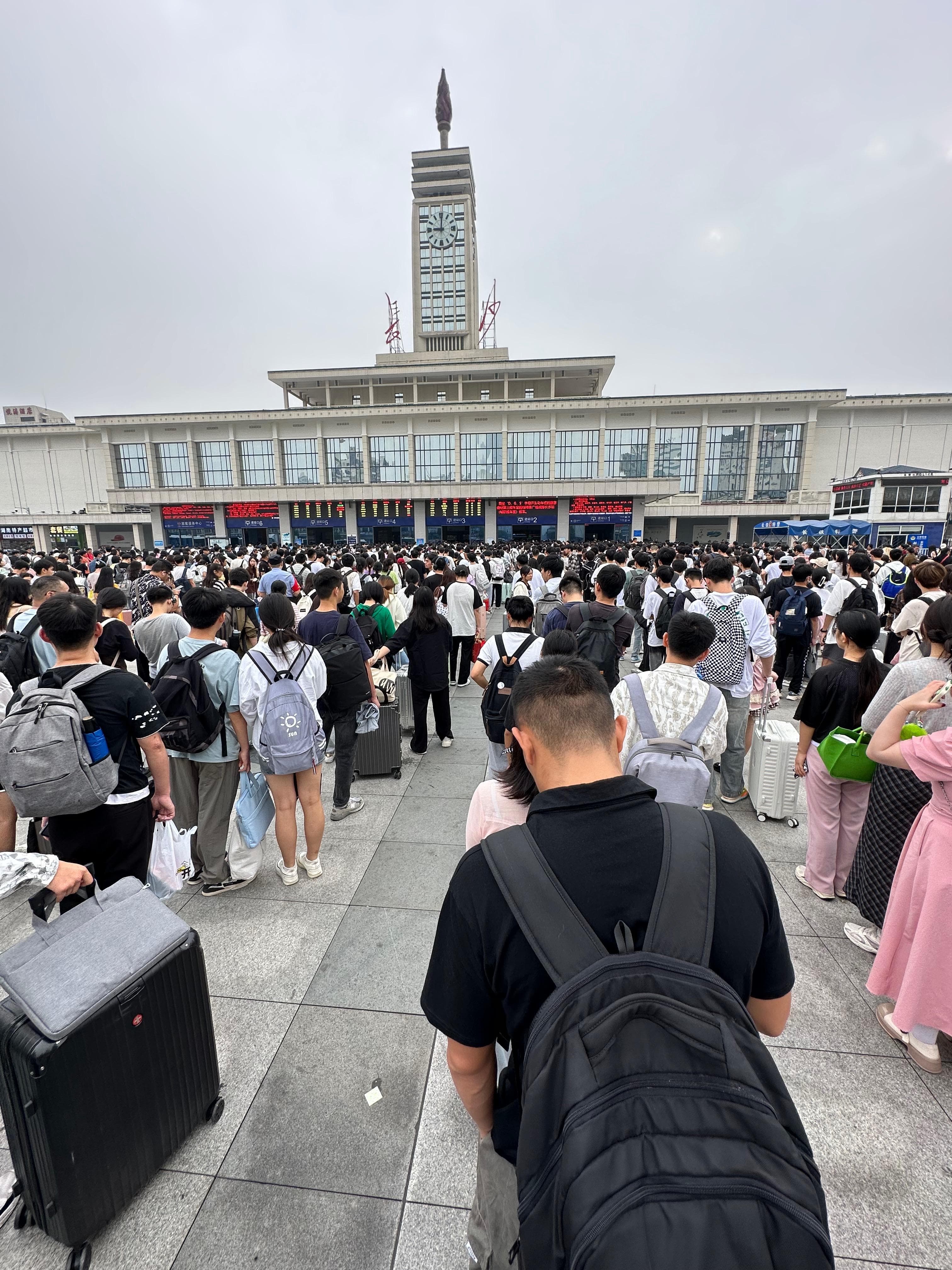 Travellers with suitcases queue outside Changsha railway station beneath its clock tower