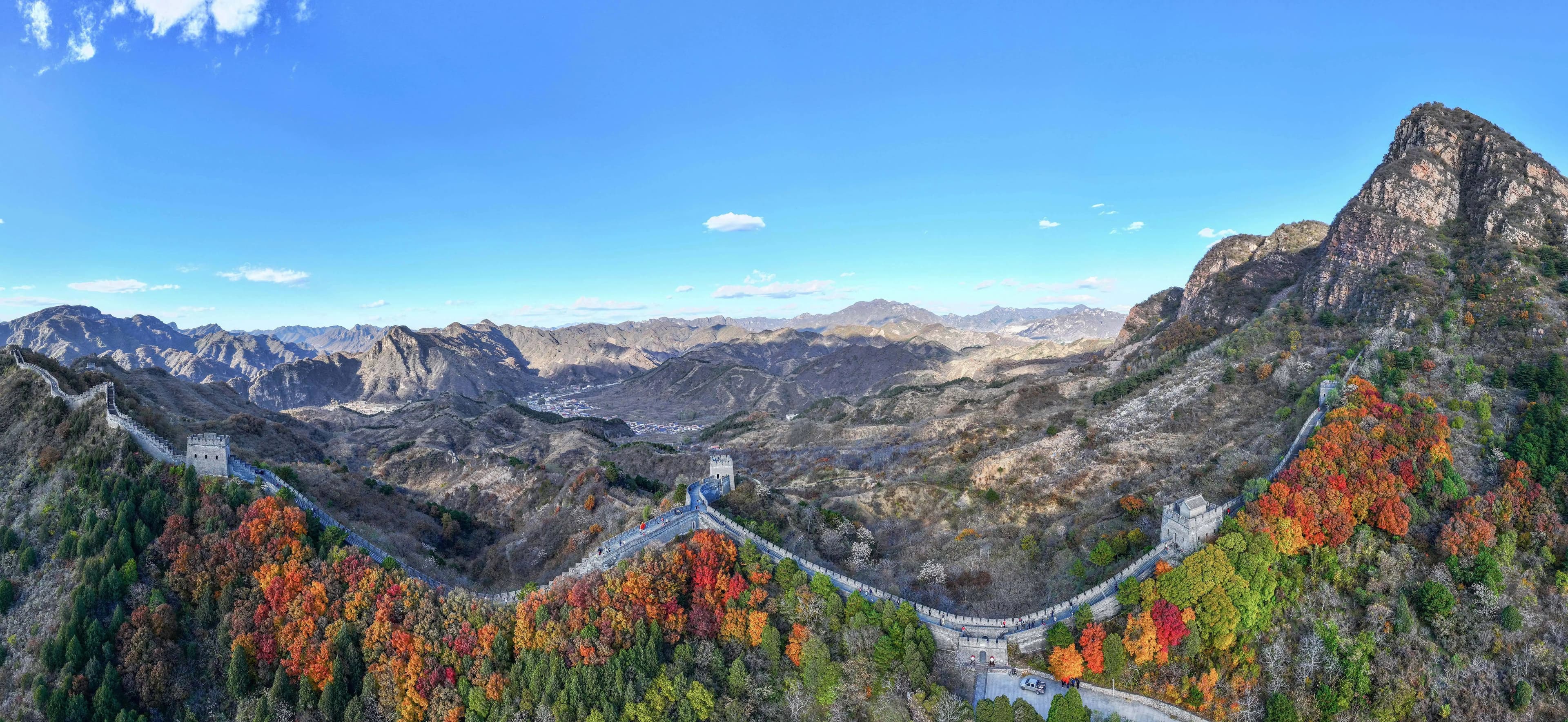 The Great Wall winds through mountain ridges above patches of red, orange and green autumn trees